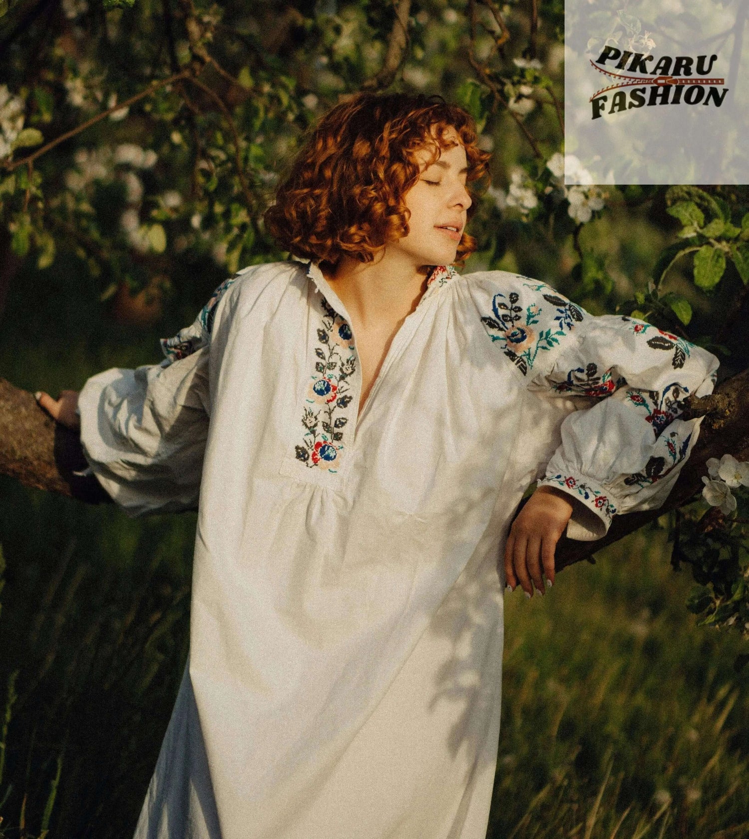 Embroidery Dress -Woman in white embroidered dress with floral patterns standing outdoors near blooming tree