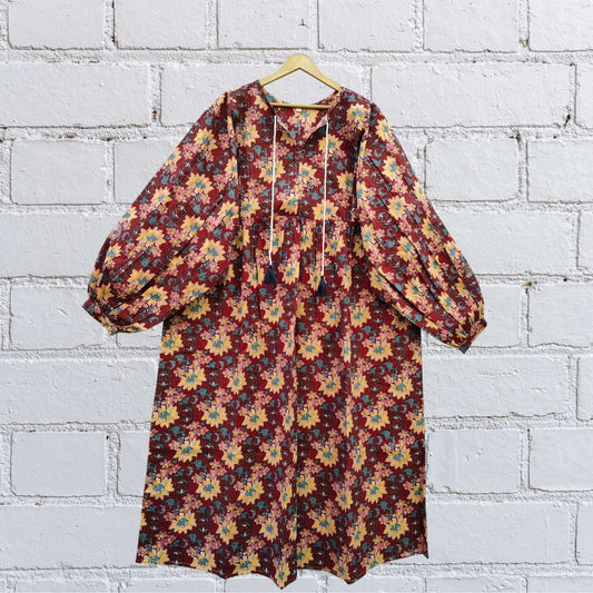 Vintage Multi-Colour Floral Boho Midi Dress with puff sleeves and tassel neck, hanging against a white brick wall.